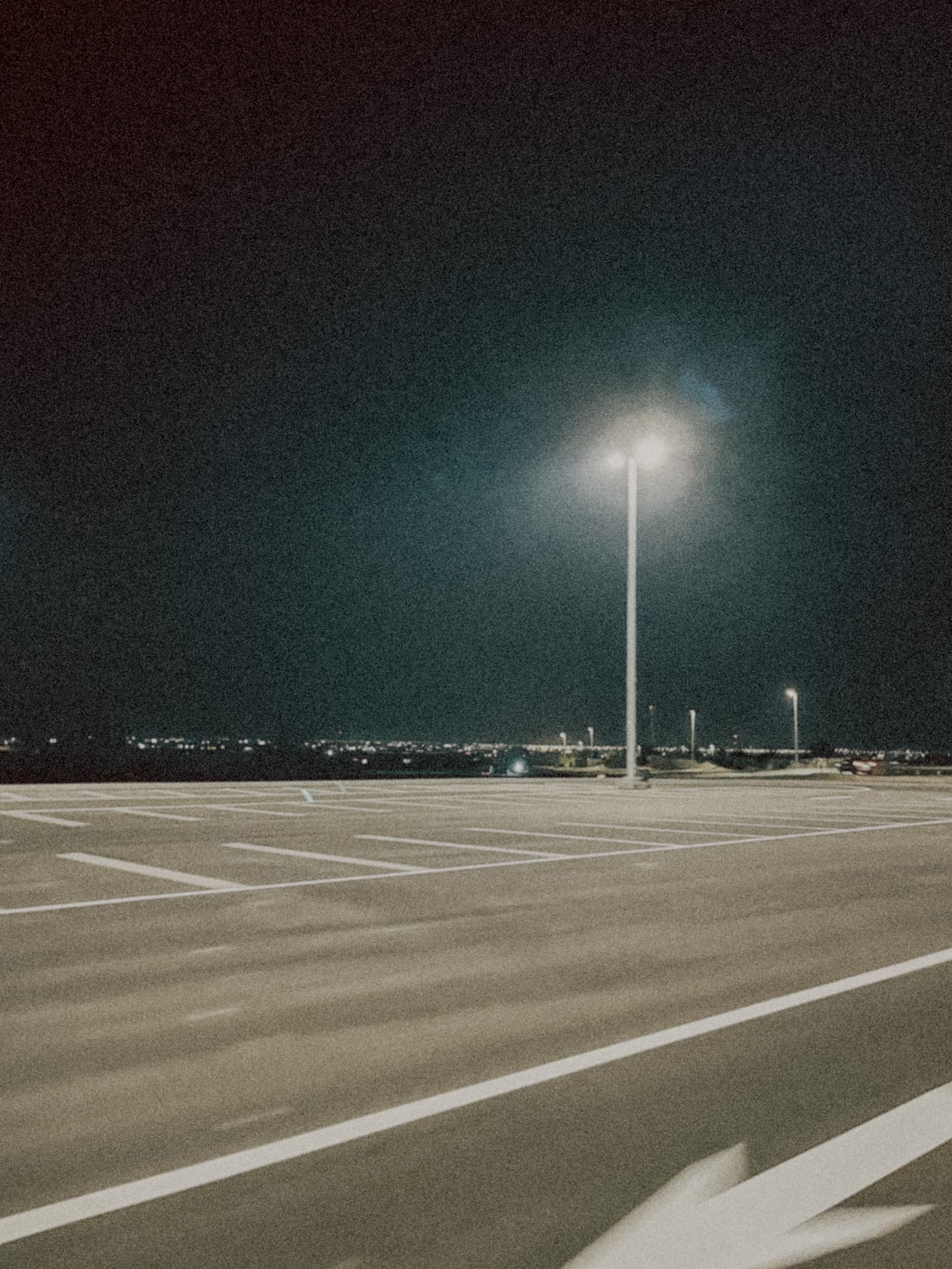 Empty Parking Area with a single streetlight with lights in the far distance.